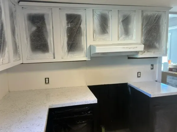 Kitchen countertops resurfaced with a speckled white stone-look finish, cabinets masked